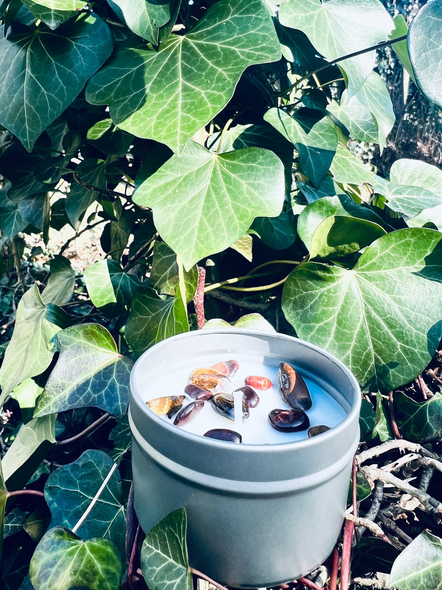 Bougie parfumée 'Oeil du Tigre' de Onéotéa - Éveil des Sens, entourée de verdure luxuriante avec une vue rapprochée sur des pierres symboliques, évoquant une atmosphère de protection et de bien-être.