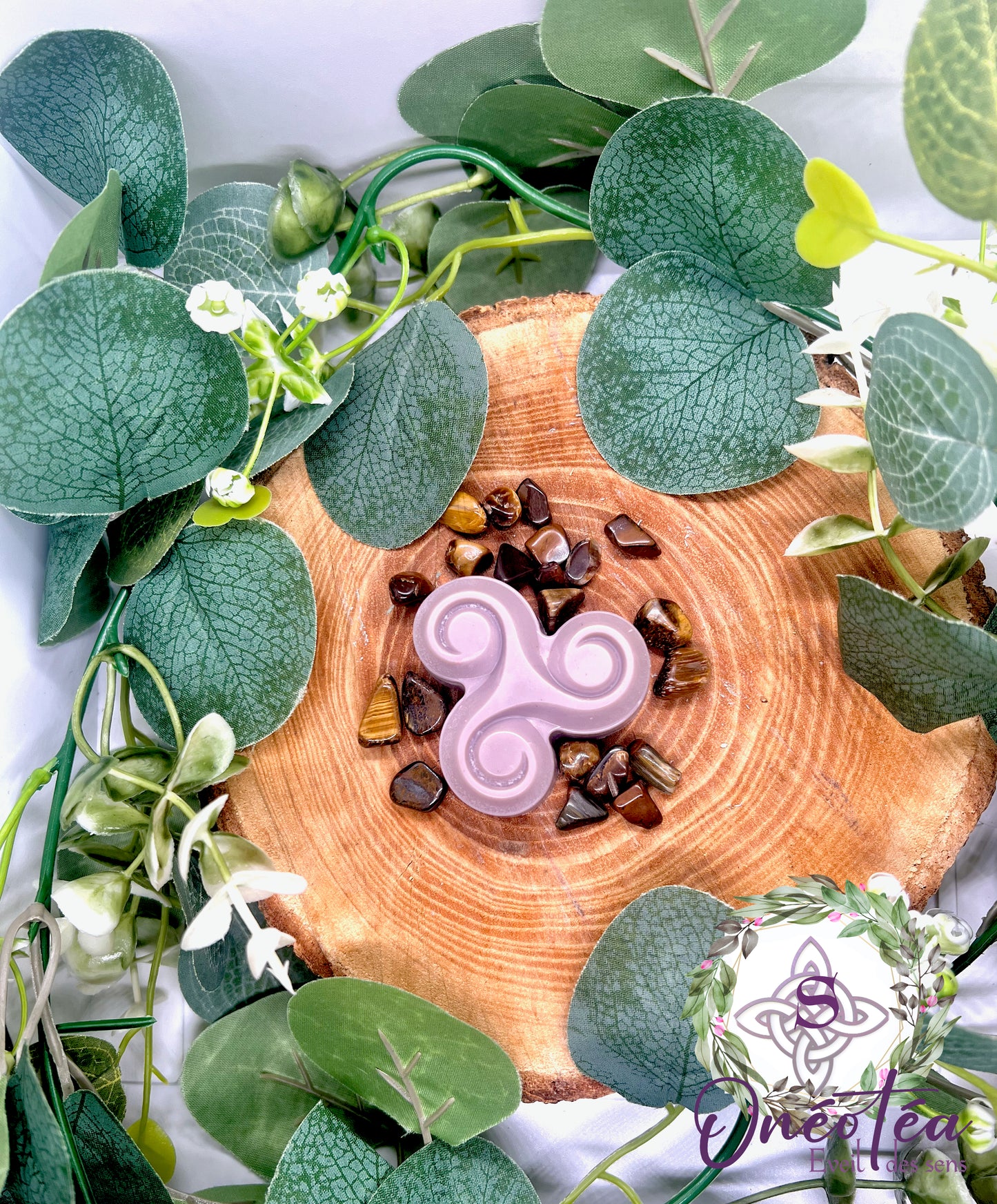 Fondant Triskel rose, posé sur un tronc de bois, accompagné de pierres naturelles et de feuilles vertes, créant un décor apaisant.