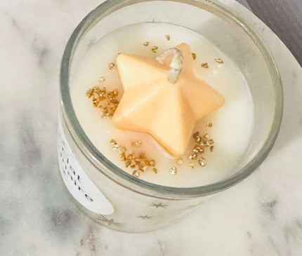 Bougie parfumée Éclat Lunaire aux notes fruitées, florales, ambrées et vanillées dans un verre élégant avec paillettes d'or.