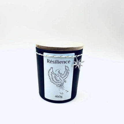 Bougie Résilience dans un pot en verre noir, couvercle en bois clair et étiquette blanche ornée d’un phénix.