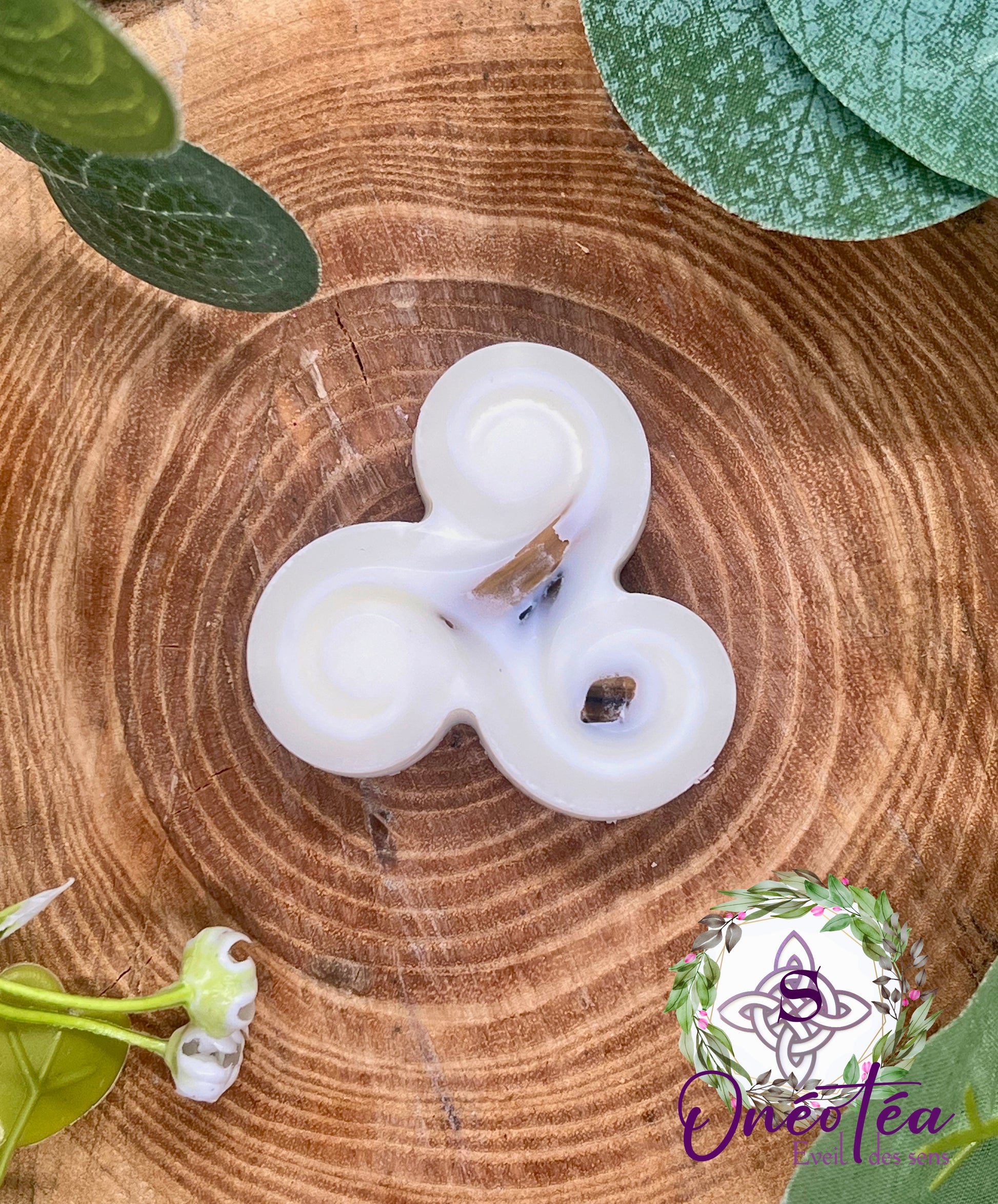 Fondant Triskel blanc sur une surface en bois, entouré de feuilles vertes, évoquant une atmosphère de sérénité et de protection.