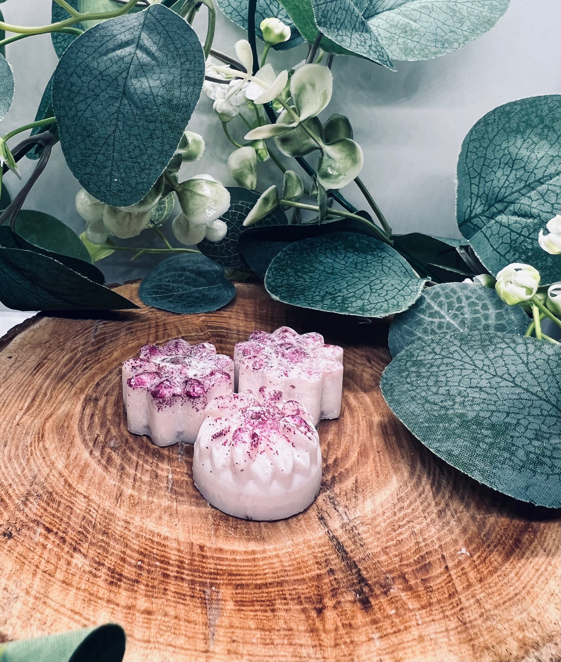 Gros plan sur trois fondants en forme de fleurs, avec des reflets brillants, disposés élégamment sur une surface en bois. Une invitation à la méditation à chaque senteur !