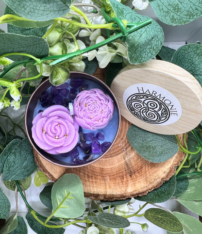 Bougie 'Harmonie du Soi' avec deux roses violettes empreintes de douceur, accompagnée de pierres d'améthyste, en harmonie avec un décor floral.