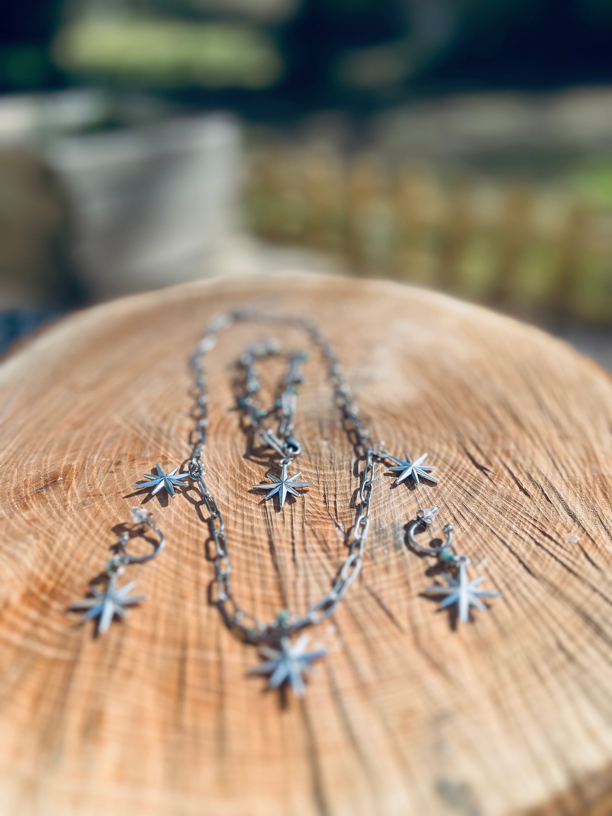 Vue d'ensemble de la parure 'Résilience' en acier inoxydable, sur une surface en bois. Le collier et les boucles d'oreilles, tous deux ornés d'étoiles, sont présentés de manière artistique, illustrant le mélange de modernité et d'élégance dans ce bijou.