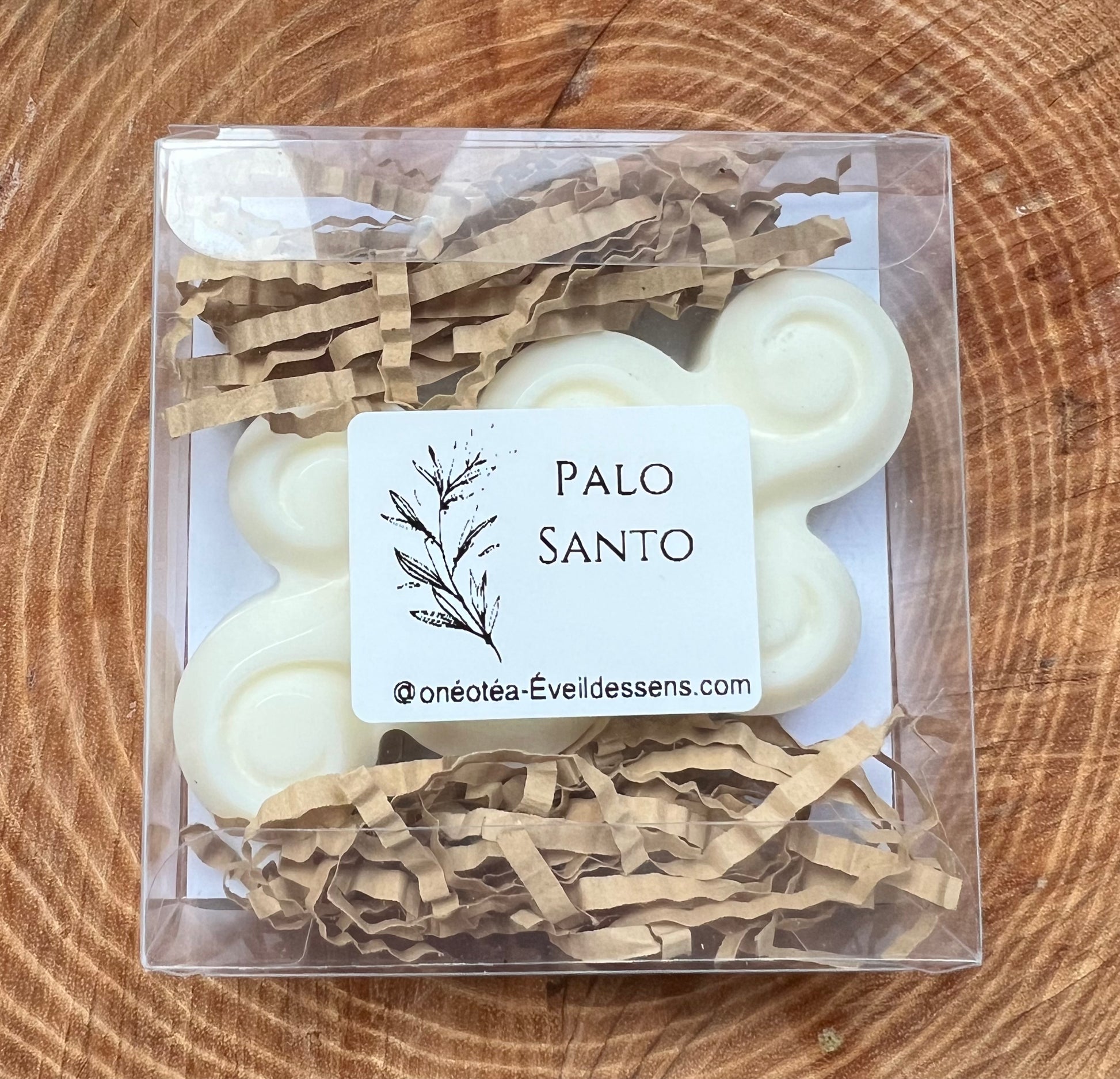 Boîte transparente contenant des fondants parfumés Triskel au Palo Santo, sur un fond de bois texturé.