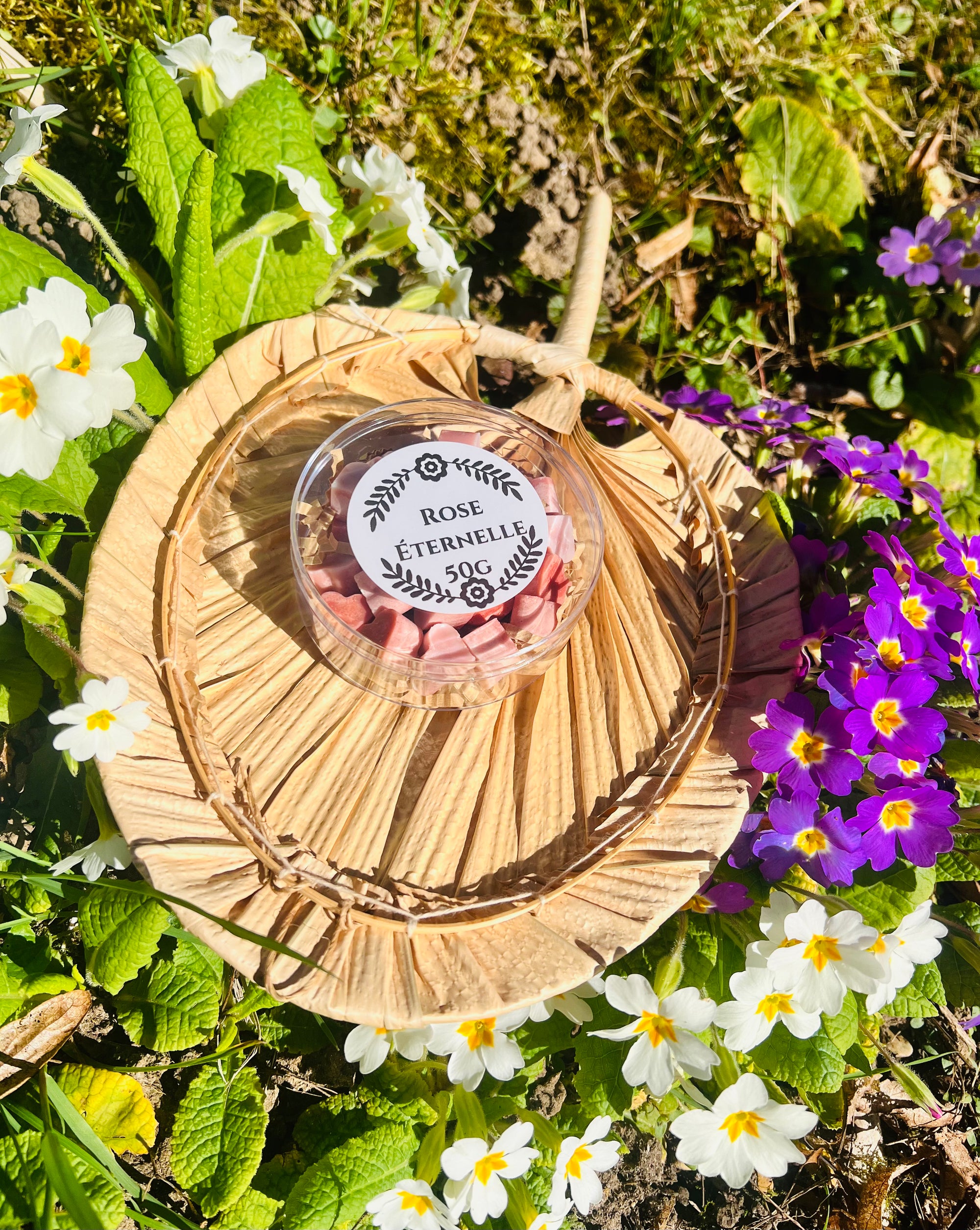 Boîte élégante contenant les fondants parfumés 'Rose éternelle' de la marque Onéotéa - Éveil des Sens, posée sur un support naturel en osier, entourée de fleurs blanches et violettes, idéale pour évoquer une ambiance douce. Ces fondants, en forme de coeur, apportent une touche parfumée à l'environnement.