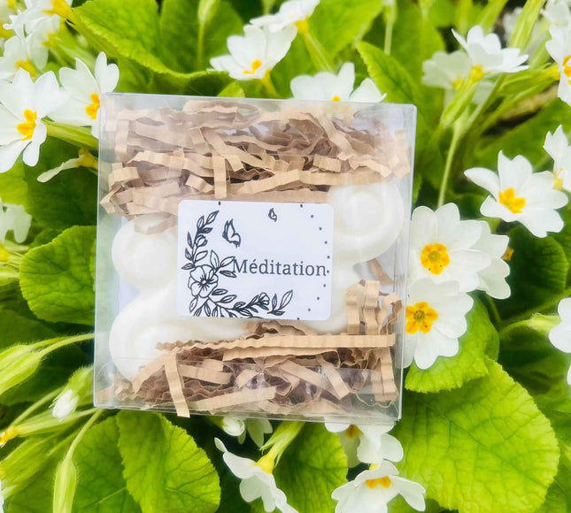 Fondants Méditation en cire blanche, présentés en lot dans une boîte transparente avec calage en papier kraft et étiquette illustrée