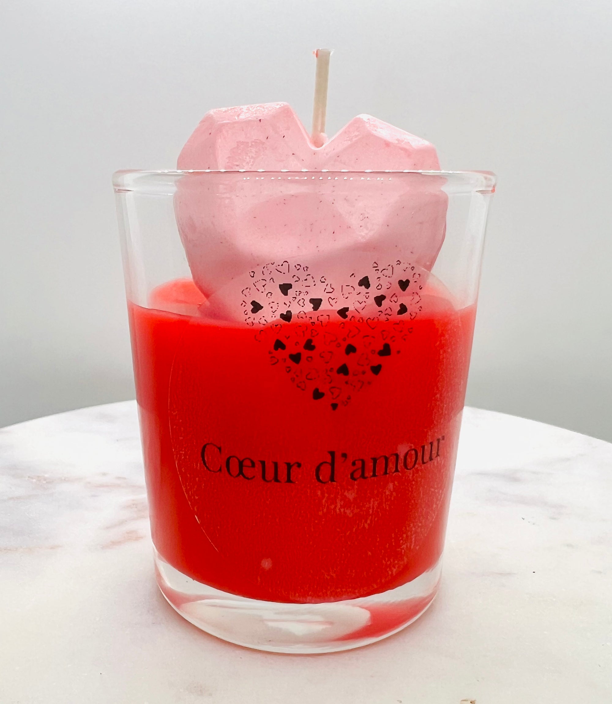 Bougie parfumée Coeur d'amour d'Onéotéa - Éveil des Sens, avec une décoration en forme de cœur en rose sur le dessus, reposant sur une surface en marbre, pour apporter une ambiance chaleureuse.