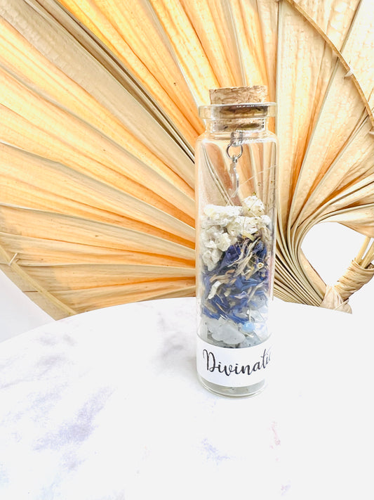 Fiole de divination de Onéotéa, ornée de pierre de lune et fleurs bleues, sur une table en marbre, prête à révéler vos secrets spirituels.