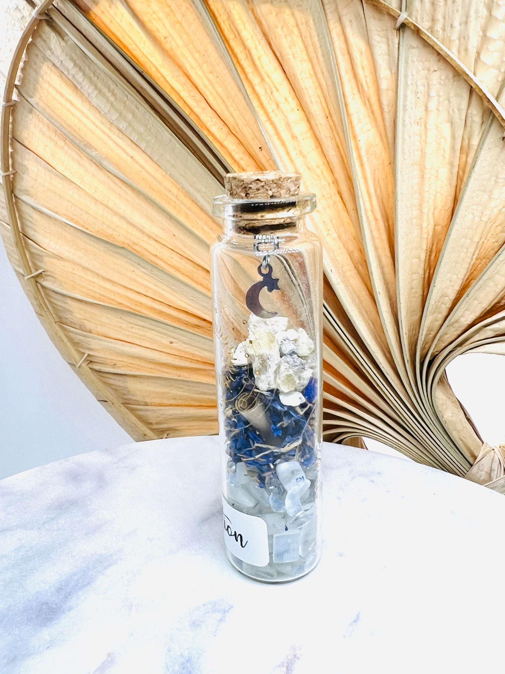 Fiole de divination de Onéotéa avec une lune suspendue, remplie de matériaux spirituels, posée sur une table marbrée, pour des moments de méditation.