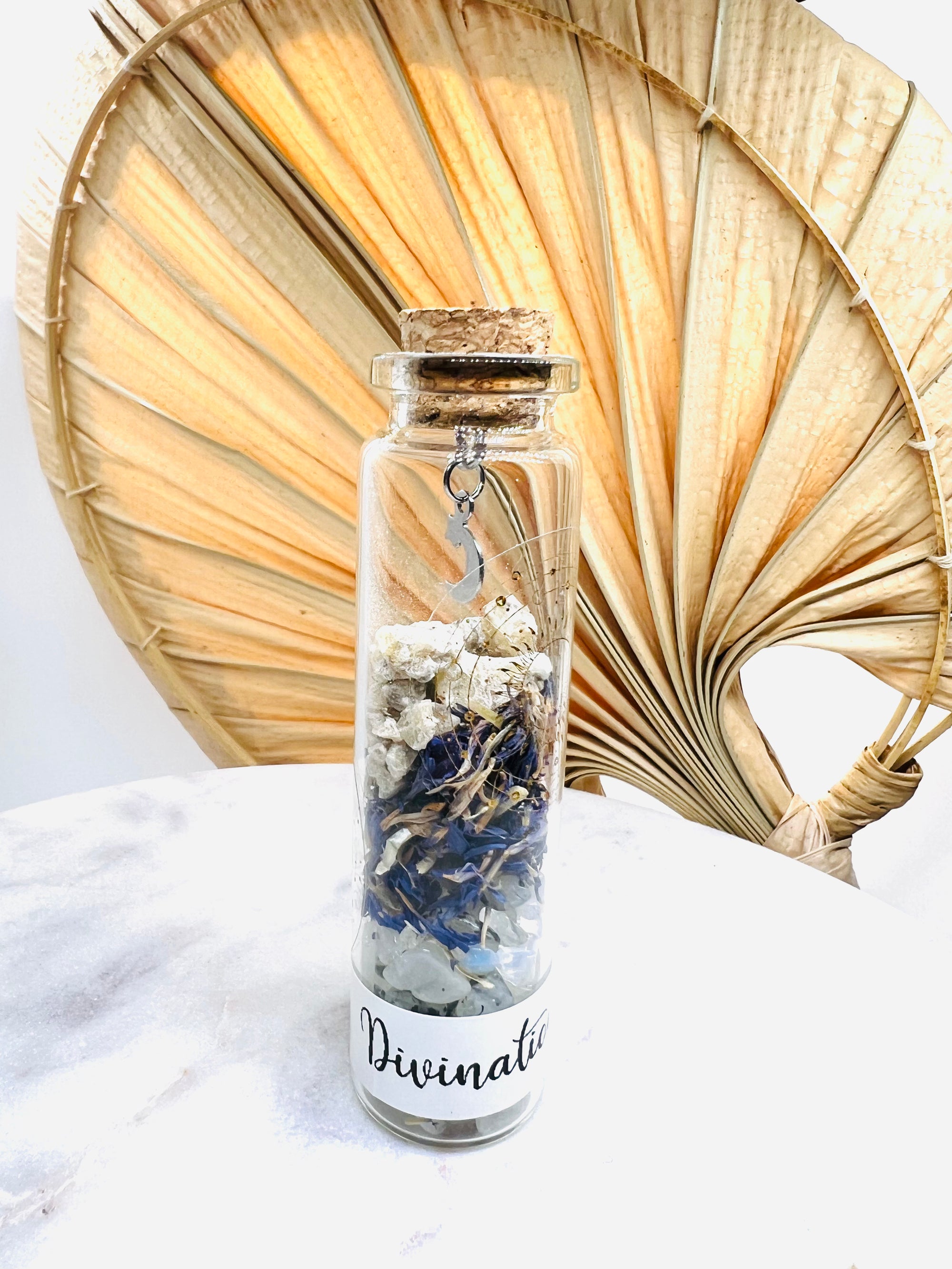 Fiole de divination de Onéotéa, pleine de mystère avec pierre de lune et bleuet, décorée d'une lune, sur une belle table, idéale pour les rituels.