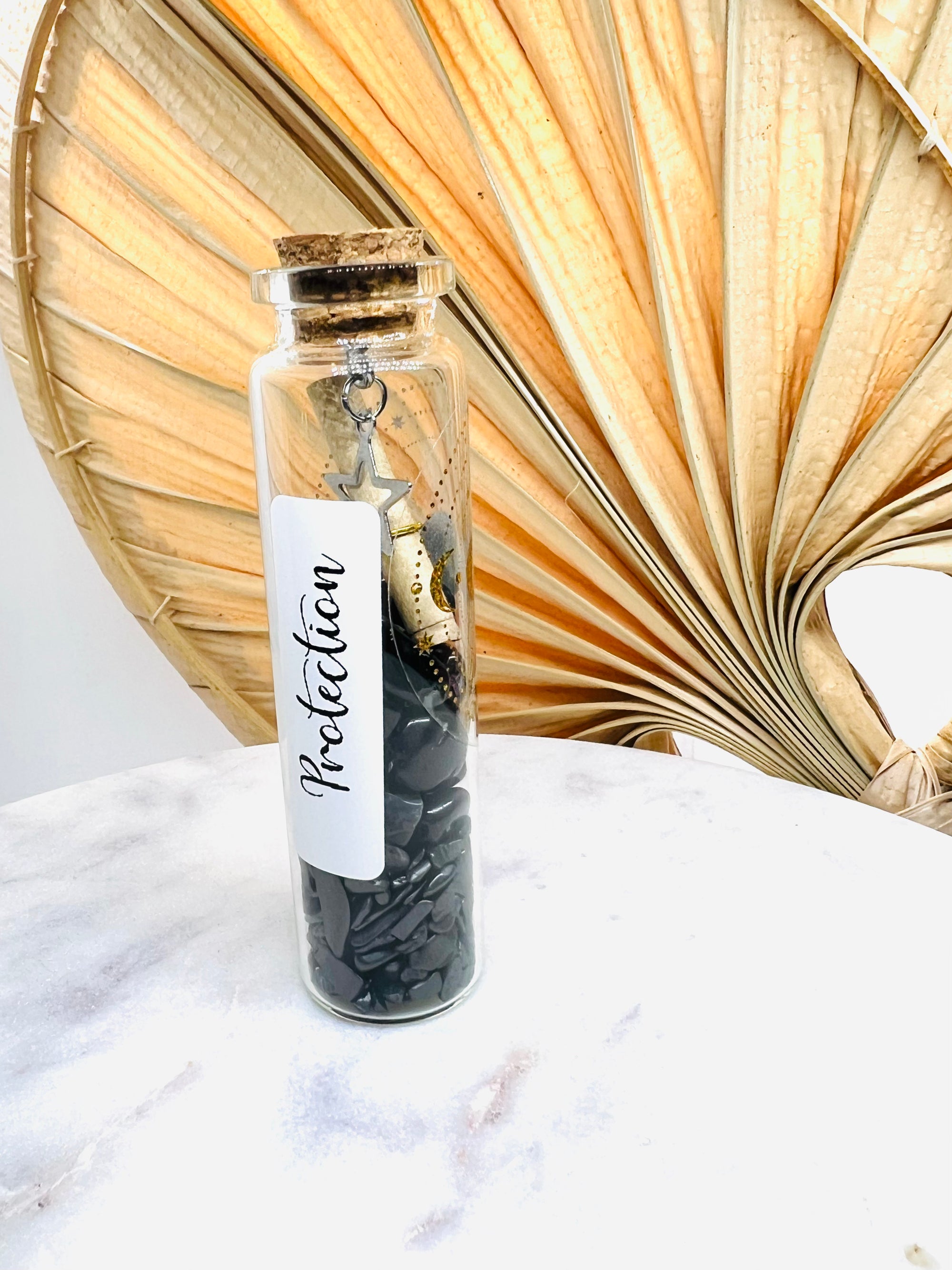 Fiole de protection en verre d'Onéotéa – Éveil des Sens, remplie de shungite brute et d'obsidienne noire, accompagnée d'un mantra sacré, le tout pour une dose de vibrations positives.