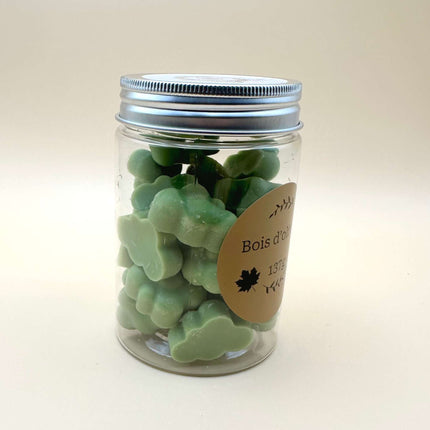 Fondants Bois d'Olivier vert pâle, moulés en petites formes irrégulières et présentés dans un pot transparent à couvercle argenté.