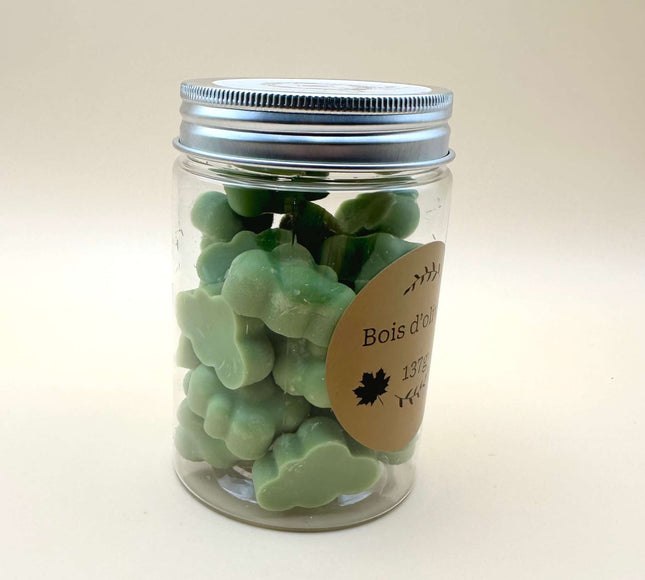 Fondants Bois d'Olivier vert pâle, moulés en petites formes irrégulières et présentés dans un pot transparent à couvercle argenté.