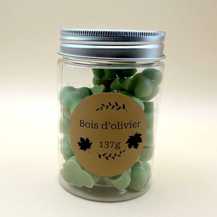 Fondants Bois d'Olivier en galets de cire végétale vert sauge, présentés dans un pot transparent à couvercle argenté.