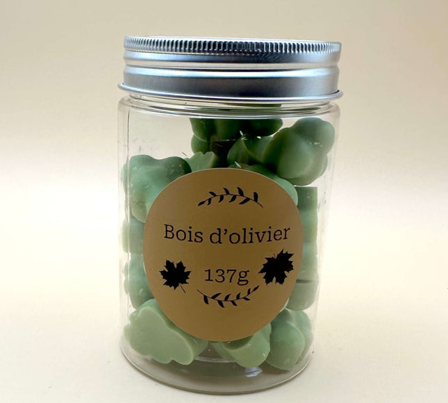 Fondants Bois d'Olivier en galets de cire végétale vert sauge, présentés dans un pot transparent à couvercle argenté.